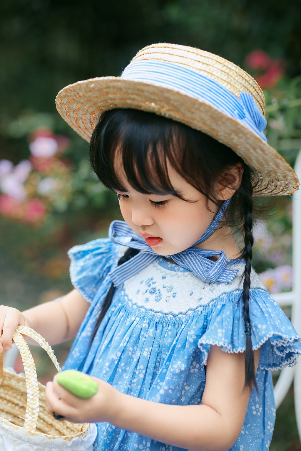 Toddler in blue smocked dress sitting in garden scene